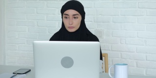 穆斯林女商人在办公室用电脑工作。一名戴着黑色头巾的妇女在阿拉伯世界的金融行业工作，使用笔记本电脑、智能手机以及其他技术