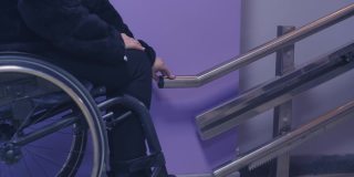 一位坐轮椅的残疾妇女在机械升降机上爬楼梯。