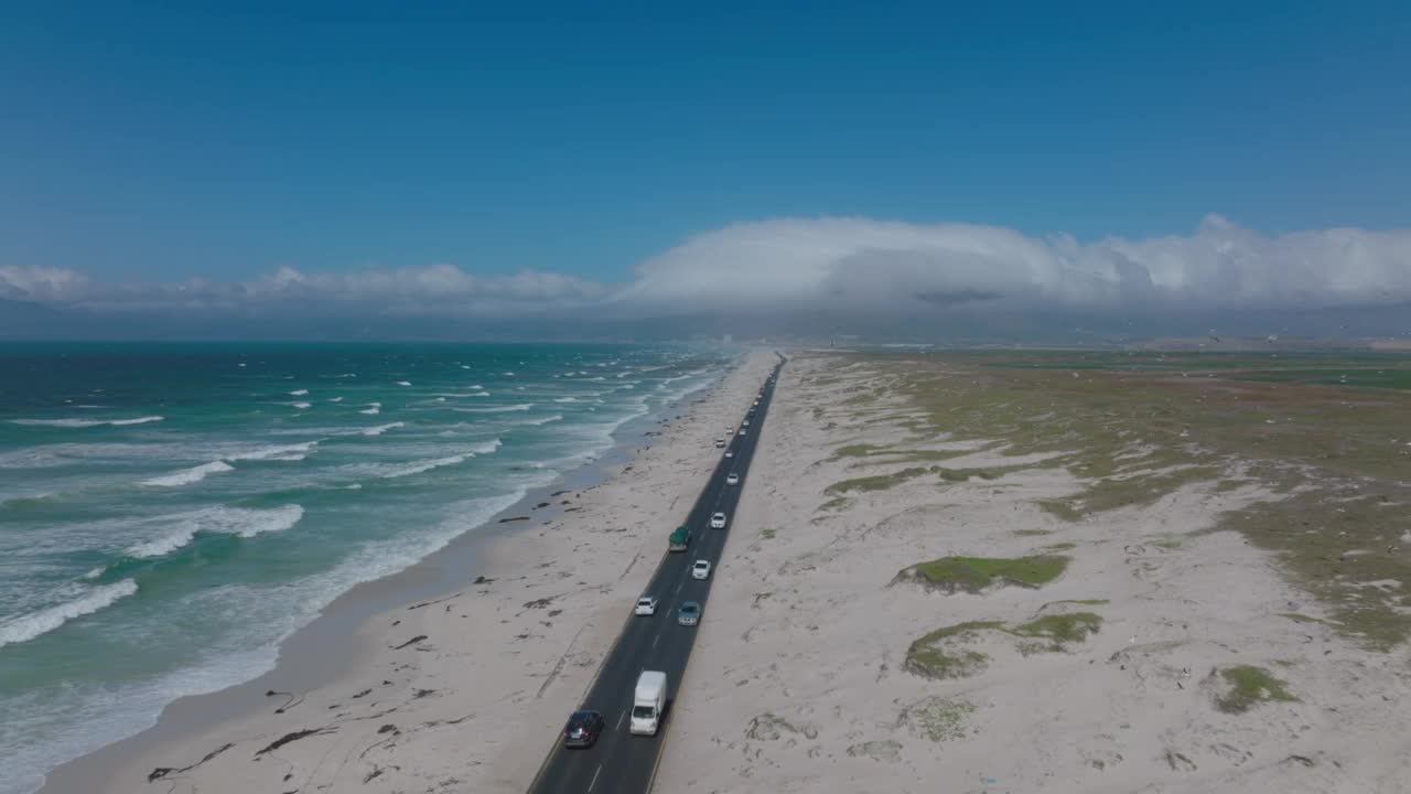 向前下降，在繁忙的沿海公路上空飞行。阳光明媚的一天在沙地景观。一群鸟在周围飞来飞去