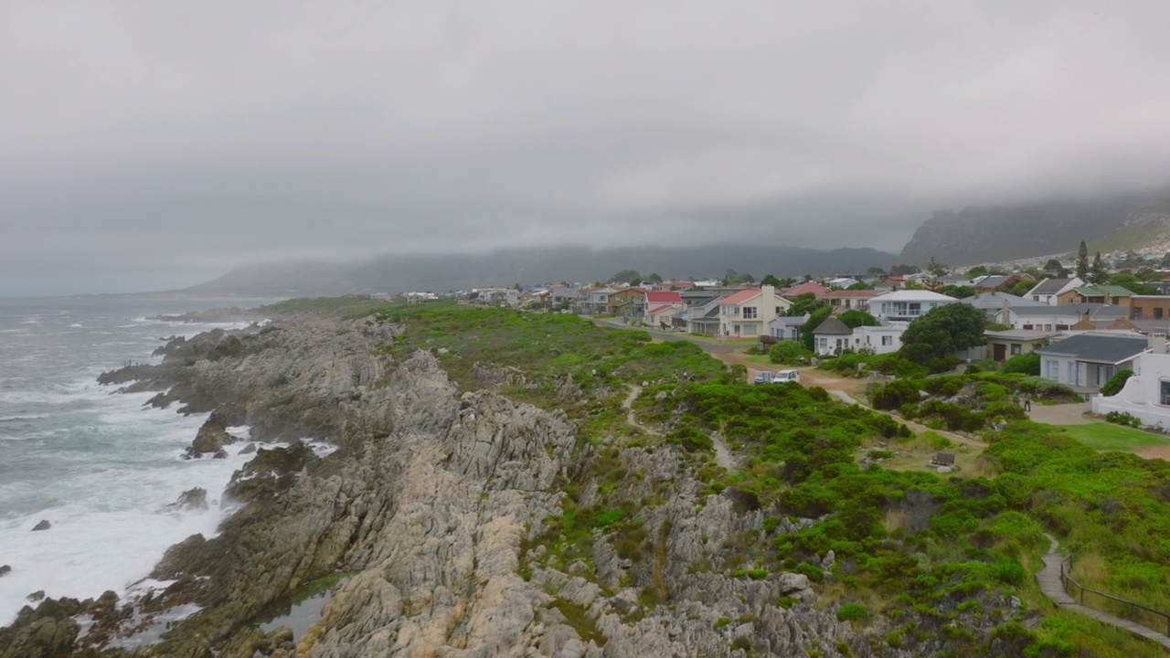 从鸟瞰图中可以看到海浪撞击海岸岩石。向前飞的景观和城镇的房子