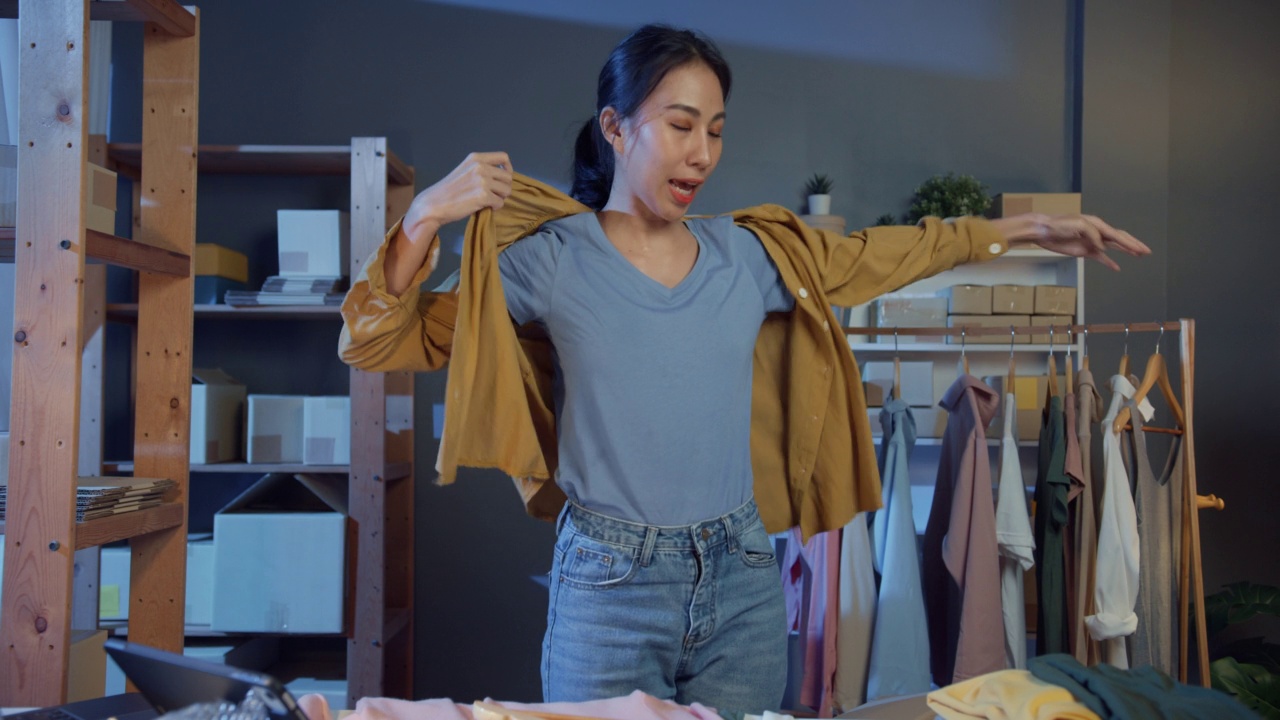 专业的吸引人的年轻的亚洲女士老板与休闲的平板电脑直播展示新系列生产与客户在商店的订单在夜间交谈。网上小企业的概念。
