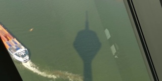 视频中，一艘集装箱船正在离港，Düsseldorf莱茵塔的影子在莱茵河畔的水面上