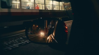 在一个欧洲小城市的夜晚，一辆经过的有轨电车在停着的汽车的后视镜里的倒影