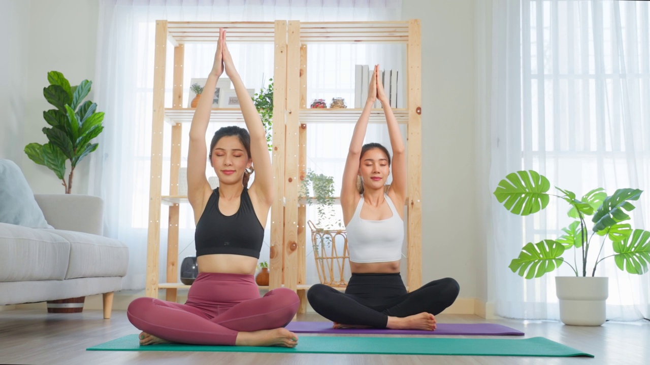 詳情圖-亞洲女性朋友一起在家做瑜伽普拉提。迷人的女孩穿著運(yùn)動(dòng)服，用墊子在家里的客廳里度過自由的休閑時(shí)光，進(jìn)行保健運(yùn)動(dòng)。