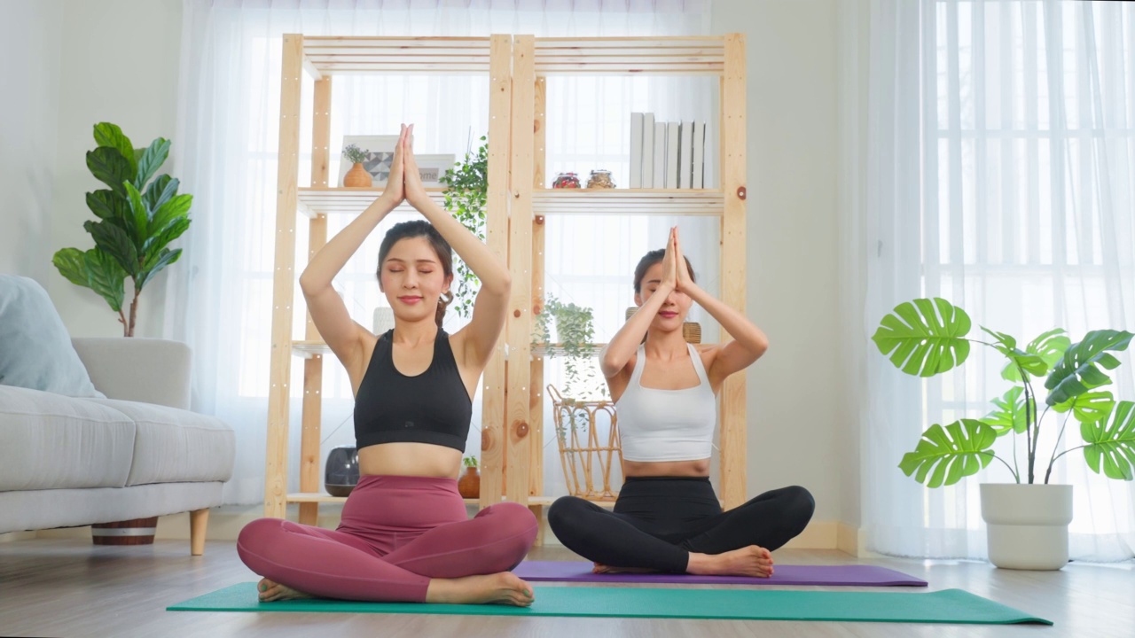 詳情圖-亞洲女性朋友一起在家做瑜伽普拉提。迷人的女孩穿著運(yùn)動(dòng)服，用墊子在家里的客廳里度過自由的休閑時(shí)光，進(jìn)行保健運(yùn)動(dòng)。