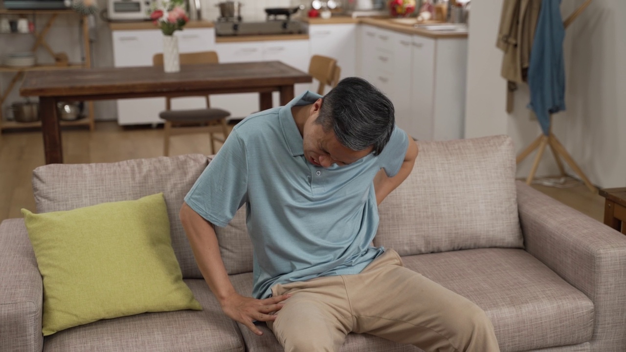 详情图-中国成熟男人坐在沙发上休息时，腰疼，呻吟，非常不舒服。老年人在家跌倒风险观念
