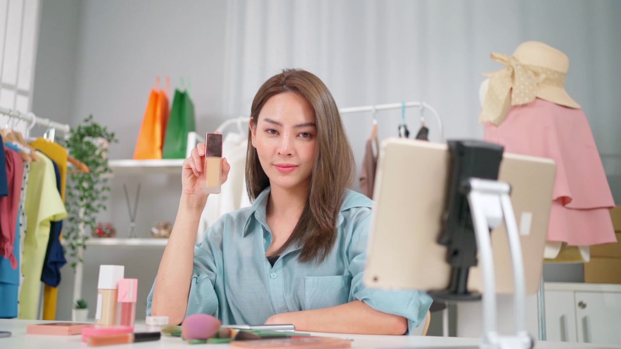 年輕的亞洲女性工作在網(wǎng)上電子商務(wù)購物在家里。創(chuàng)業(yè)在線時尚布料業(yè)務(wù)。通過使用平板電腦視頻電話設(shè)置直播，向客戶展示產(chǎn)品。買賣概念