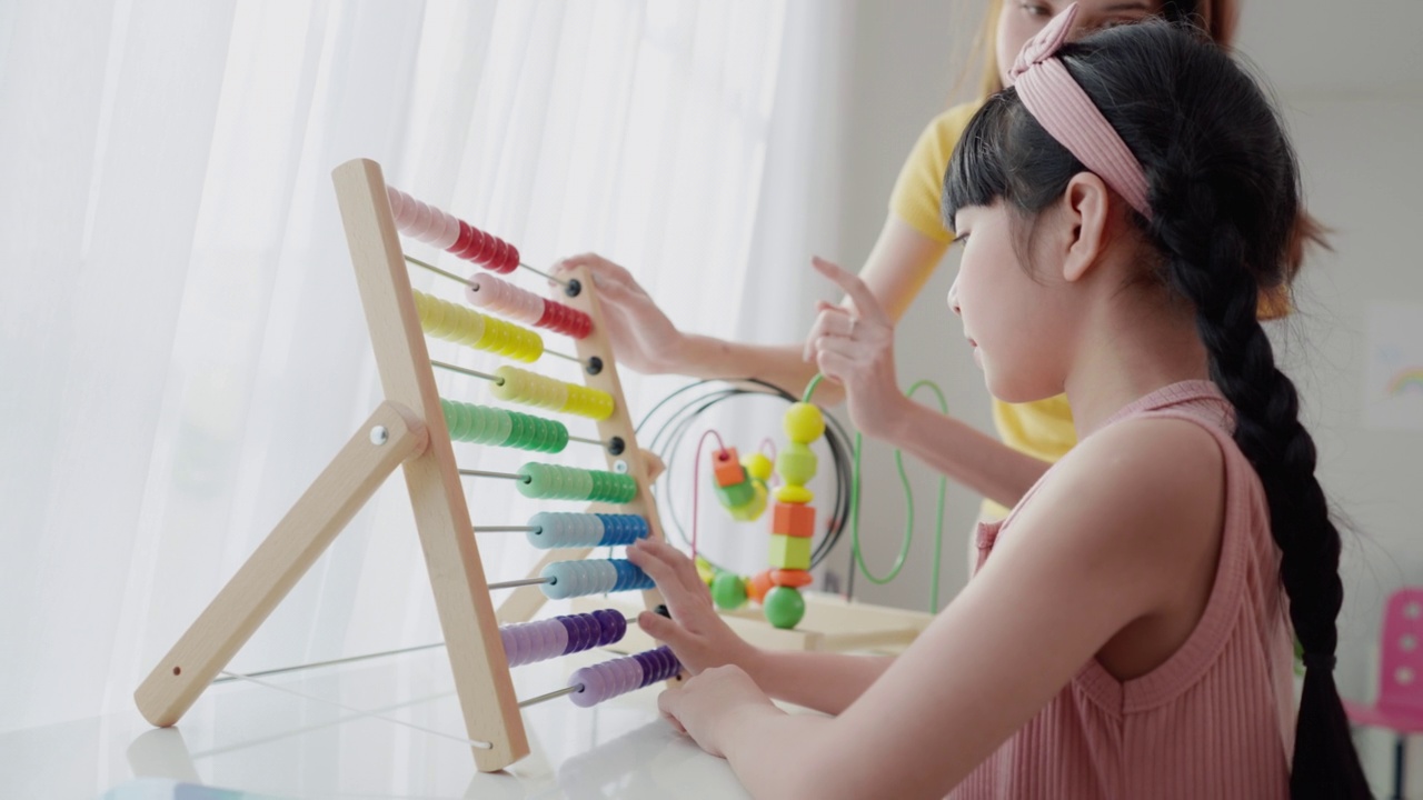 详情图-一位亚洲美女老师正在向她可爱的6岁亚洲女学生讲解如何使用彩色算盘进行计算，她将计数器沿框中代表数字的杆子滑动。数学教室。