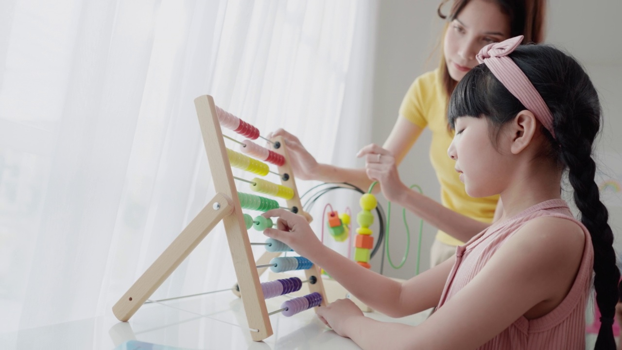 详情图-一位亚洲美女老师正在向她可爱的6岁亚洲女学生讲解如何使用彩色算盘进行计算，她将计数器沿框中代表数字的杆子滑动。数学教室。