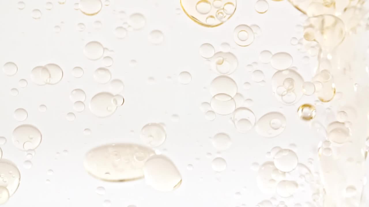移动的黄色黄金油的慢动作，空气泡泡在水中上升在淡白色的背景。含气泡的透明化妆品凝胶液。微距镜头。