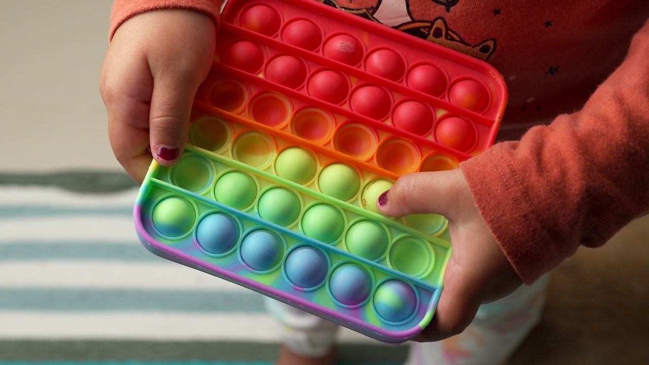小孩子在室内玩彩色Pop It玩具游戏。简单和有趣。