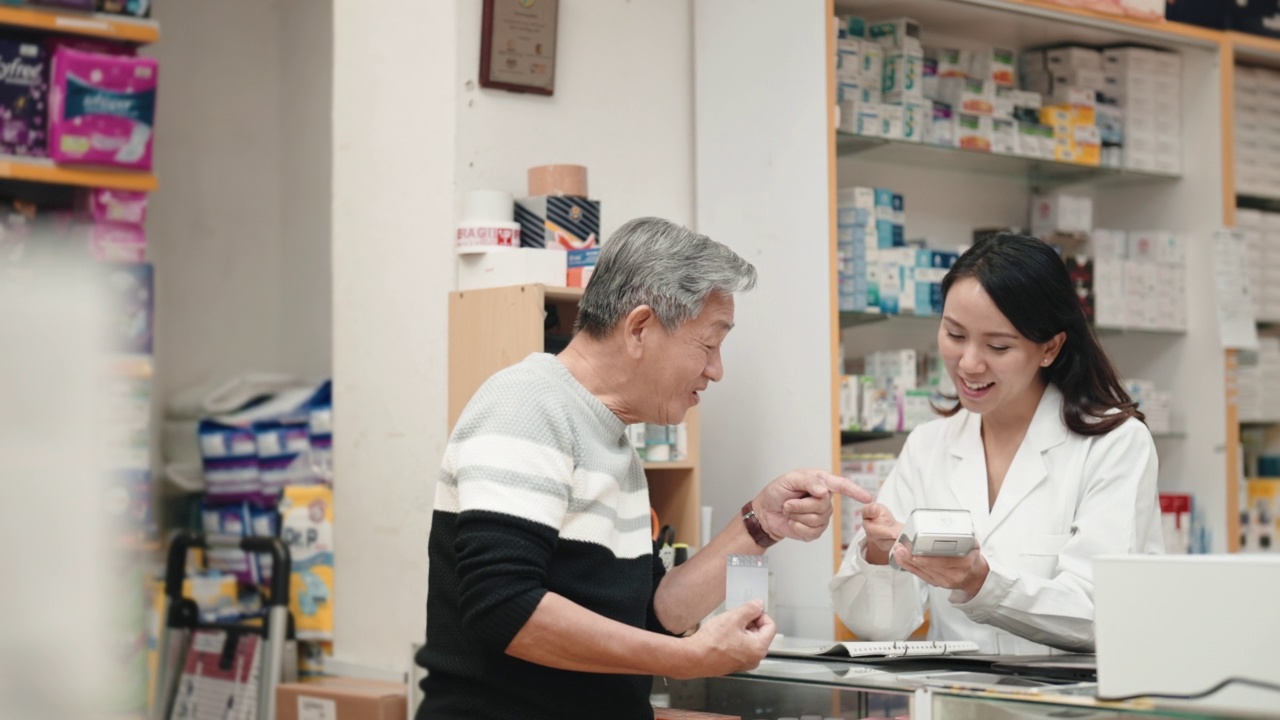 亚洲华人老人在药房柜台用信用卡支付非接触式支付