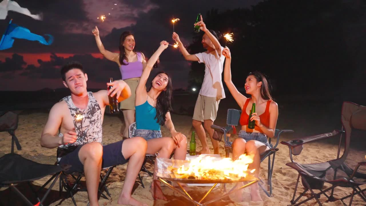 详情图-一群亚洲年轻男女晚上在海滩上聚会。迷人的朋友们在海边露营时唱歌跳舞，一起在热带海岛度假度假