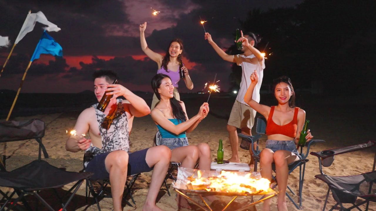 详情图-一群亚洲年轻男女晚上在海滩上聚会。迷人的朋友们在海边露营时唱歌跳舞，一起在热带海岛度假度假