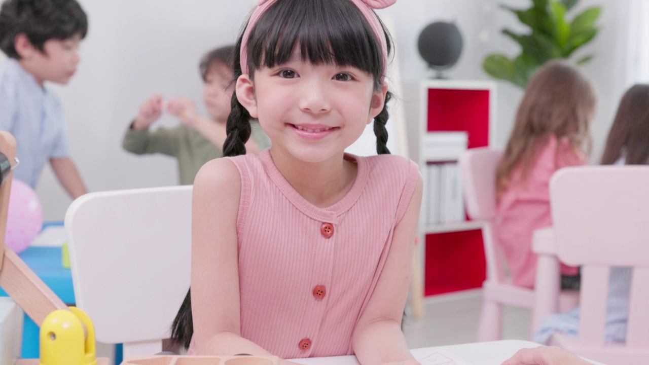 一个可爱的女孩的微笑肖像勤奋工作在幼儿园的教室与不同的聪明的孩子们