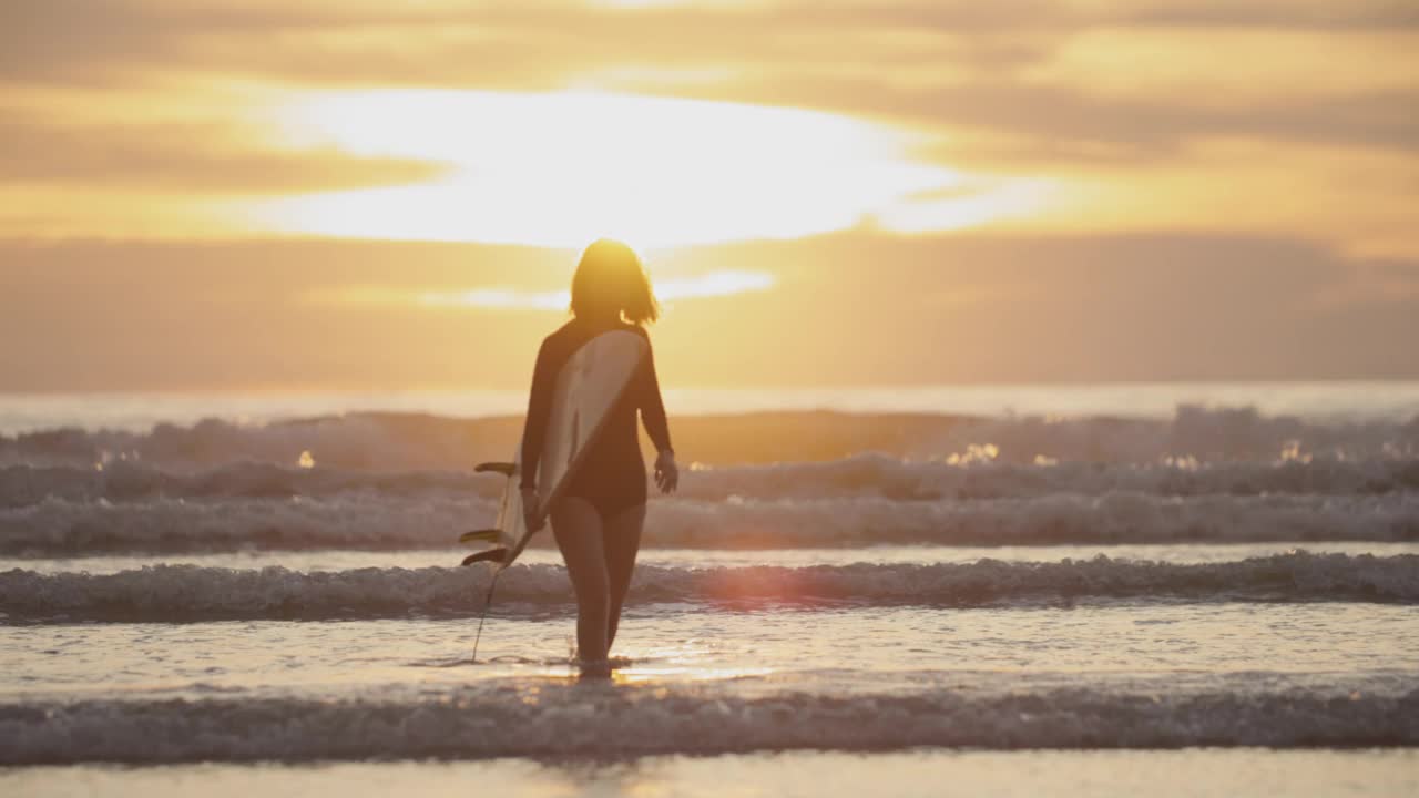 夕阳下的热带海滩上冲浪女孩的剪影。