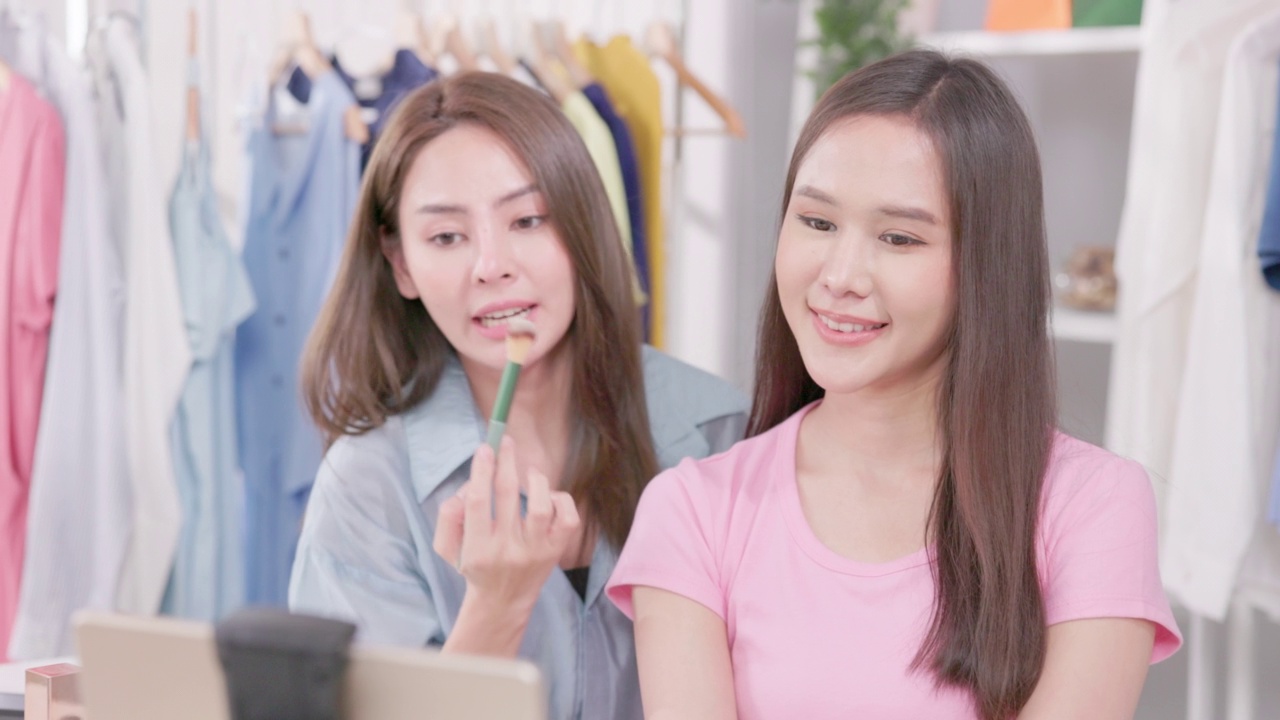 详情图-一位美妆博主正在用三脚架拍摄化妆教程。网红女人在她的家庭演播室里一边直播一边评论化妆品。这位女性视频博主用刷子涂抹皮肤