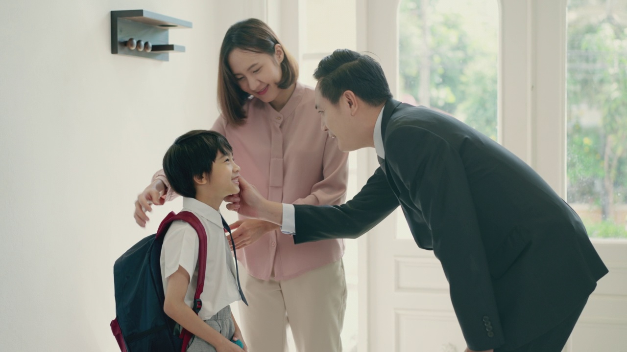亚洲人的父亲、母亲和小男孩正准备去上学，这是因新冠肺炎疫情而停课的第一天。一位亚洲爸爸正在鼓励和拥抱他的儿子，而妈妈正在为他们的儿子准备背包。
