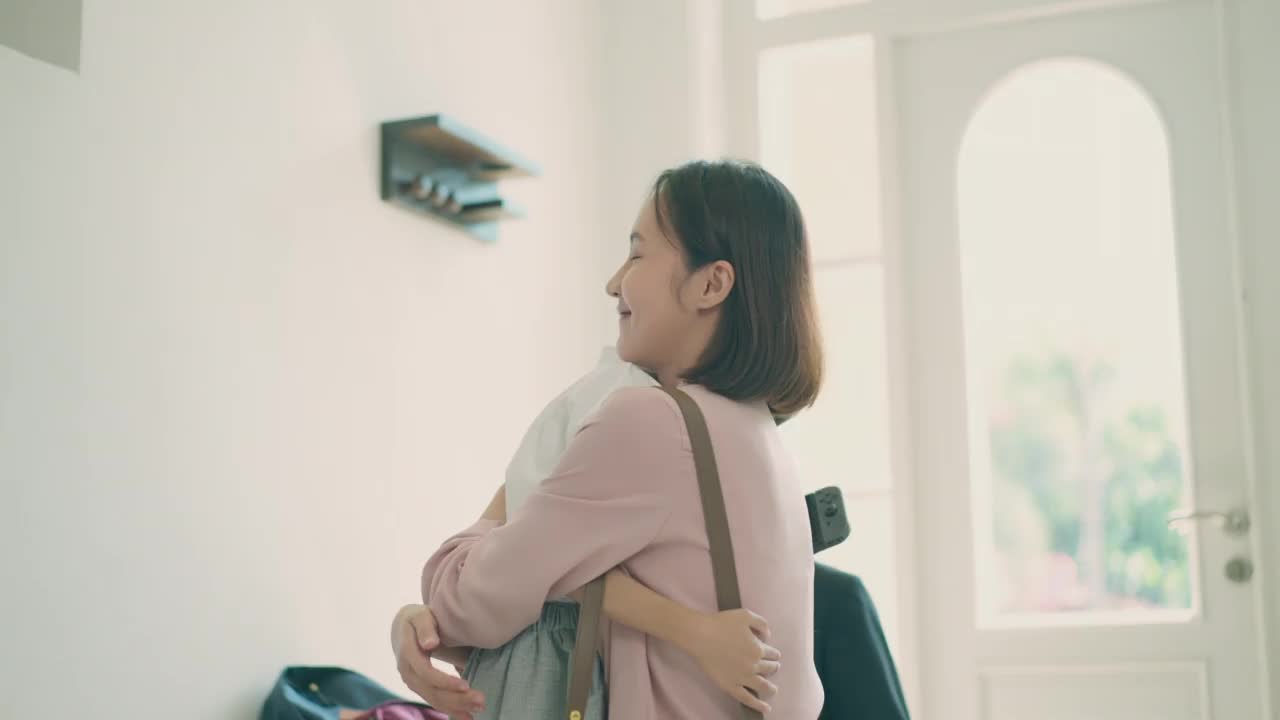 亞洲媽媽抱著她的小兒子，準(zhǔn)備送他去上學(xué)，而亞洲爸爸在家里的客廳里背著兒子的書包，準(zhǔn)備去上學(xué)。親子關(guān)系或愛與紐帶表達(dá)的概念。