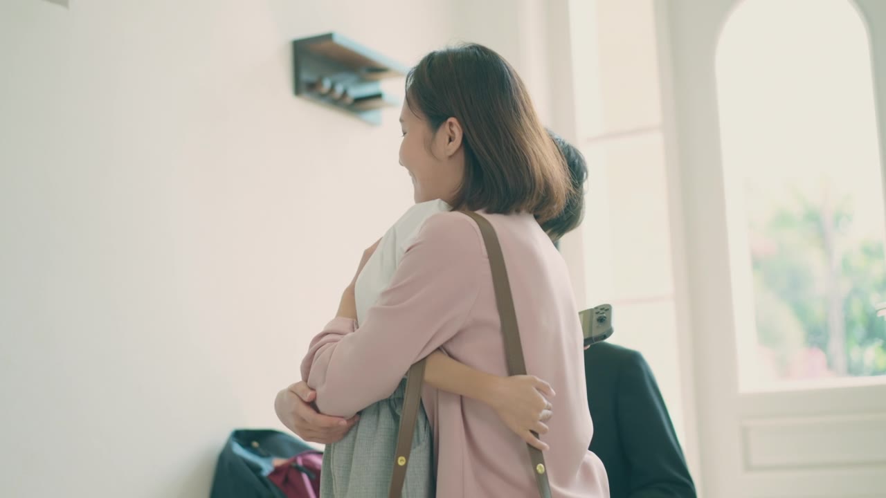 詳情圖-亞洲媽媽抱著她的小兒子，準(zhǔn)備送他去上學(xué)，而亞洲爸爸在家里的客廳里背著兒子的書(shū)包，準(zhǔn)備去上學(xué)。親子關(guān)系或愛(ài)與紐帶表達(dá)的概念。