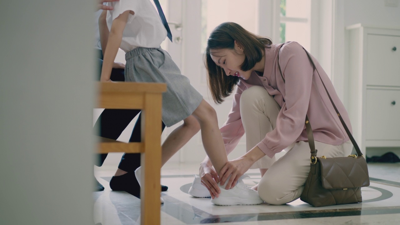 一个不知名的小男孩在家里被他的妈妈系鞋带。快乐的亚洲妈妈在早上上学前给儿子系鞋带。