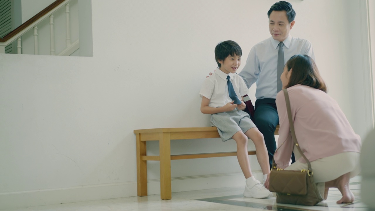 詳情圖-年輕的亞洲母親正在給她可愛的兒子穿上鞋子，而帥氣的亞洲父親坐在長凳上和他的孩子聊天，第一天上學(xué)。準(zhǔn)備上學(xué)。