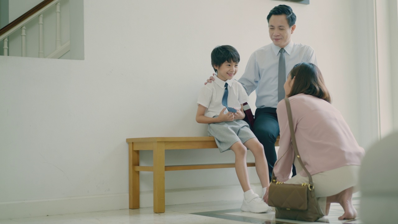 詳情圖-年輕的亞洲母親正在給她可愛的兒子穿上鞋子，而帥氣的亞洲父親坐在長凳上和他的孩子聊天，第一天上學(xué)。準(zhǔn)備上學(xué)。