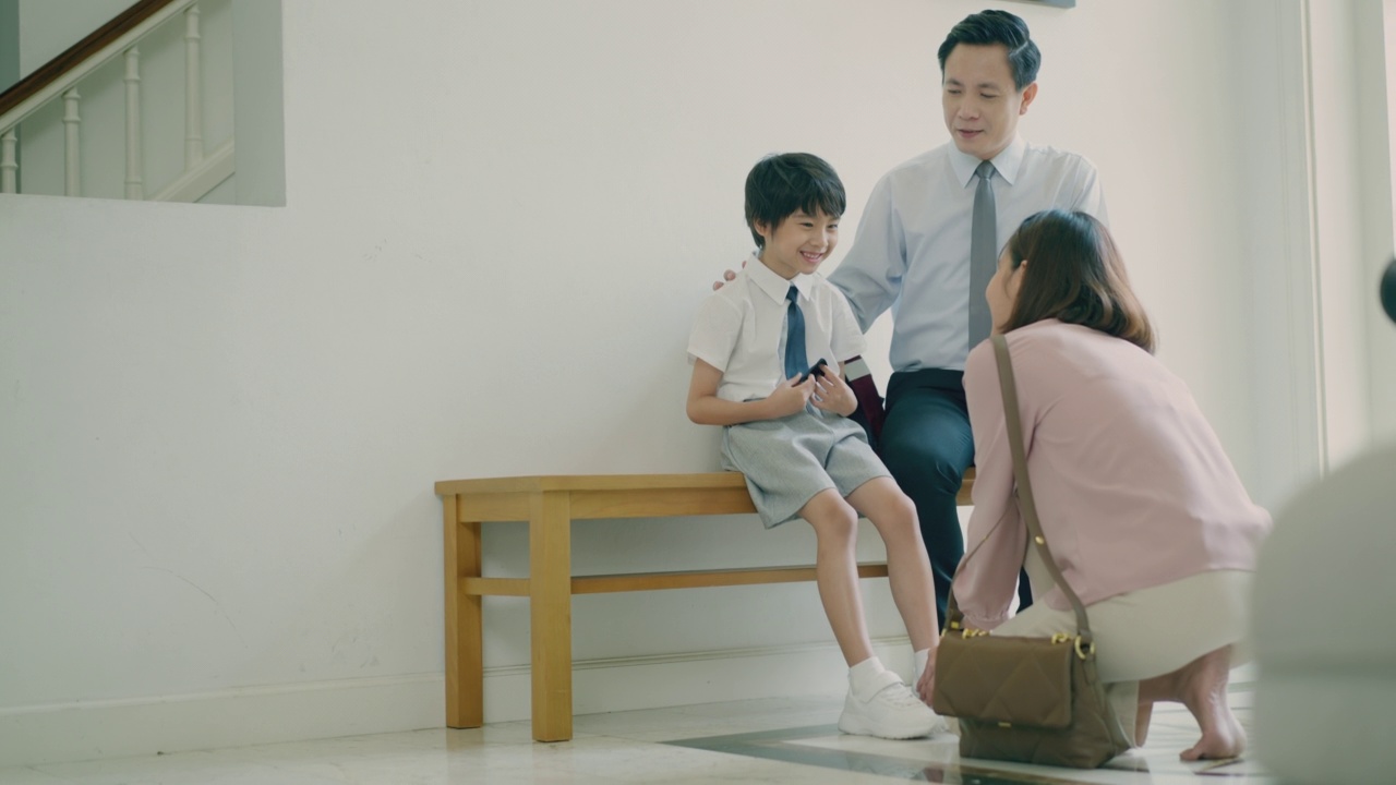 詳情圖-年輕的亞洲母親正在給她可愛的兒子穿上鞋子，而帥氣的亞洲父親坐在長凳上和他的孩子聊天，第一天上學(xué)。準(zhǔn)備上學(xué)。