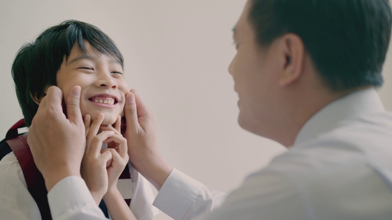 花时间在一起，亚洲父亲鼓励他的儿子享受去学校在早上触摸他的孩子的脸是微笑。早上，爸爸和小可爱在一起开心地玩耍。
