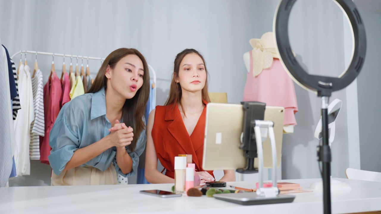 详情图-亚洲两名女性视频博主对着镜头回顾在家里的美容。美妆博主网红女性朋友在办公室商店的平板电脑上直播并展示化妆刷。