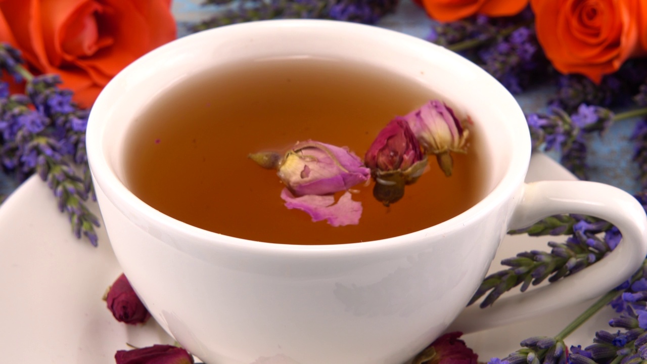 普罗旺斯风格的构图:茶与芬芳的玫瑰花蕾，新鲜的玫瑰花和薰衣草放在复古的浅蓝色木制桌面上。