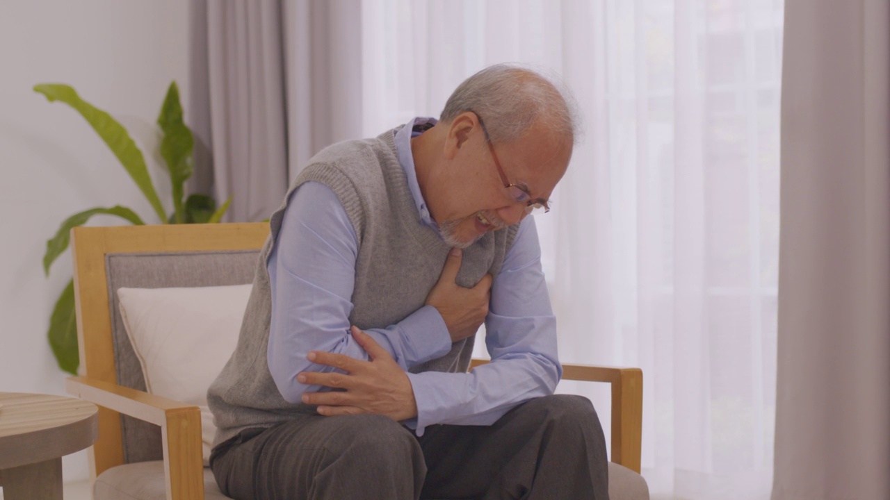 亚洲老人坐在客厅的沙发上，因心脏病胸口疼痛。