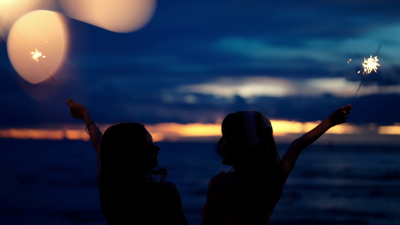 4K亚洲女性朋友在夏夜的热带海岛海滩上一起玩烟火。