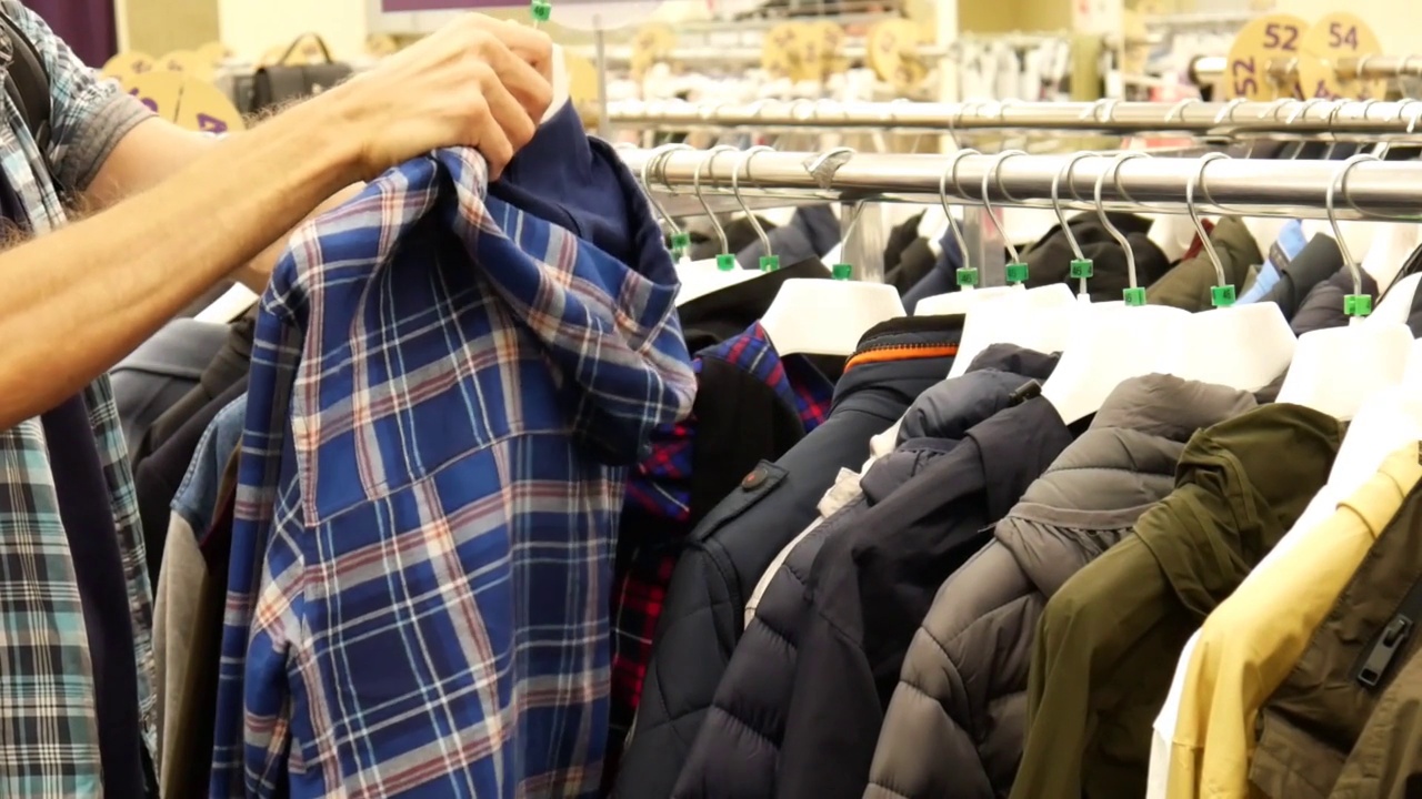 服装店货架上的一排各式各样的夹克，男顾客挑选一件方格的