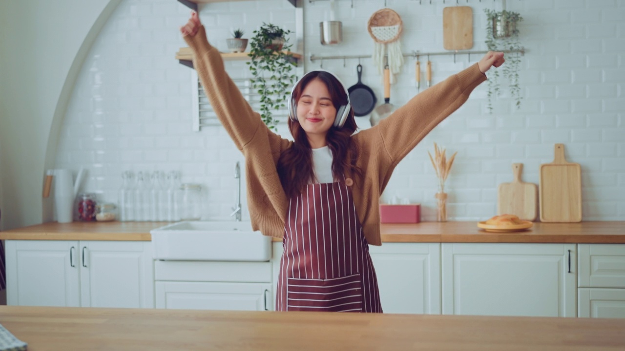 慢动作的快乐年轻的亚洲女人跳舞与耳机在家里有乐趣放松与有趣的舞蹈动作享受自由的周末早上。