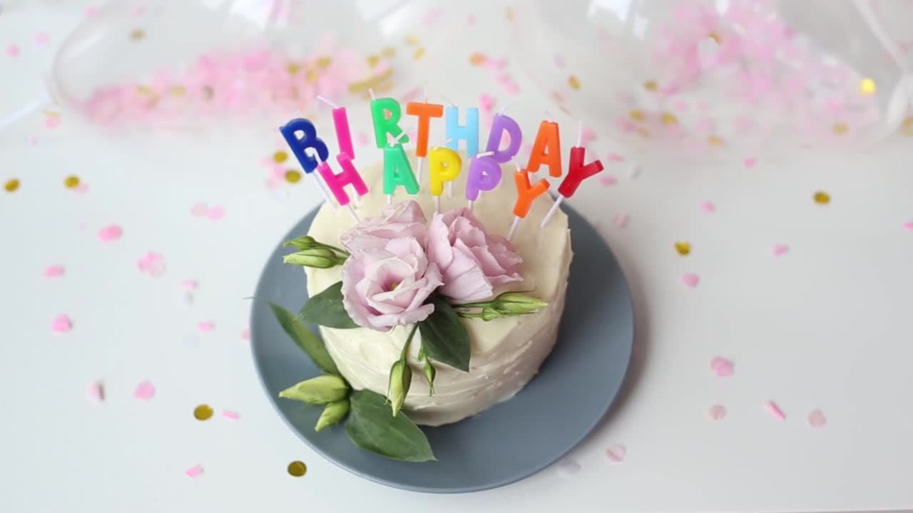 年轻女子点燃蜡烛的一个蛋糕的形式-生日快乐，并扑灭火柴。白色奶油节日派的特写镜头。生日蛋糕和燃烧的彩色蜡烛。