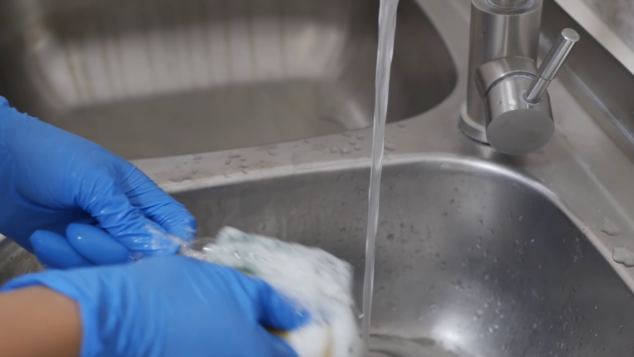 详情图-消毒:用含肥皂的海绵和水槽中水龙头的流水对牙科器械进行消毒的过程戴着蓝色手套的牙科助手的手正在清洗牙医的工作工具