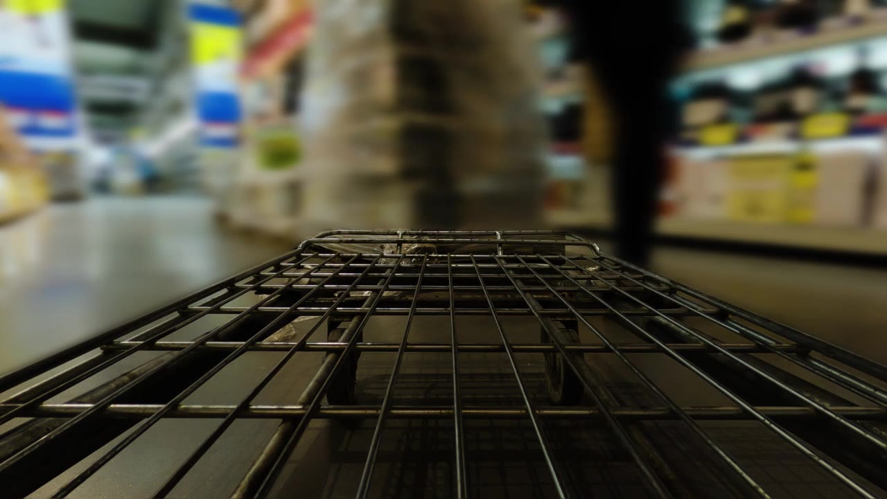 详情图-超市或仓库里的购物车在一排排货架和货架间穿行。散焦模糊背景。购物的概念。