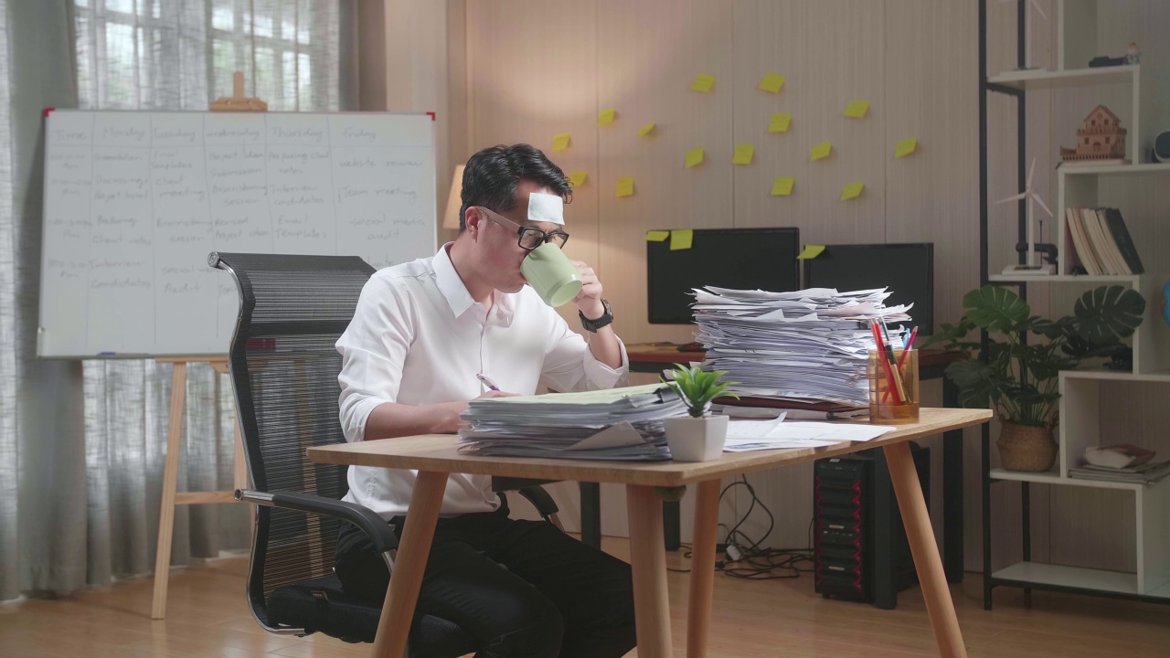 生病的亚洲人一边喝水，一边在办公室努力处理文件