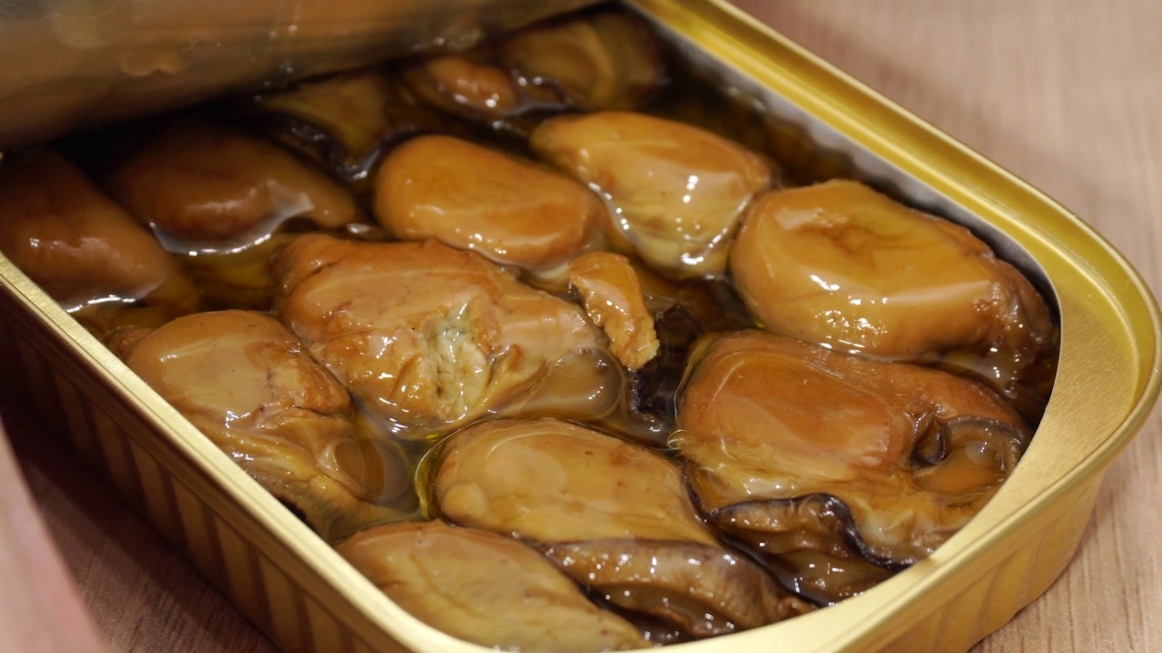 一只手打开一罐烟熏贻贝。海鲜美食理念。油浸海鲜罐头。贻贝紧紧地装在罐子里。