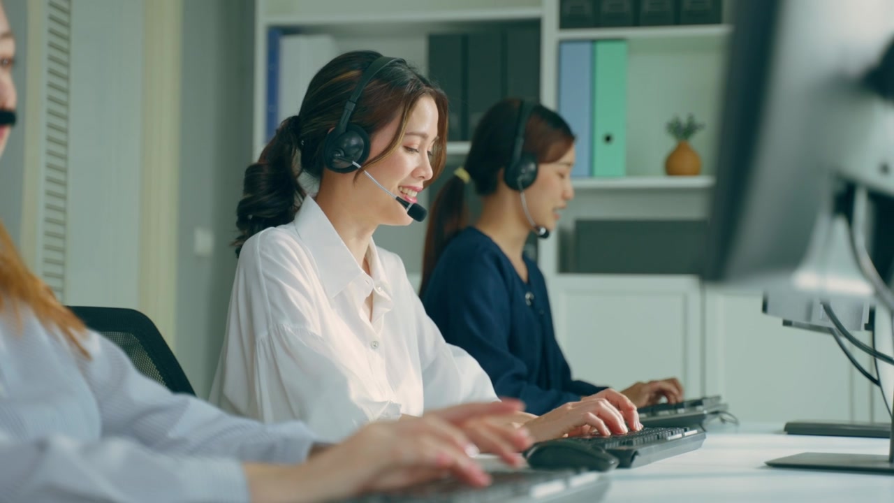 詳情圖-群美麗的商務(wù)女性呼叫中心工作在辦公室企業(yè)。漂亮的年輕員工坐在桌子上，戴著耳機(jī)，使用筆記本電腦在工作場(chǎng)所支持客戶