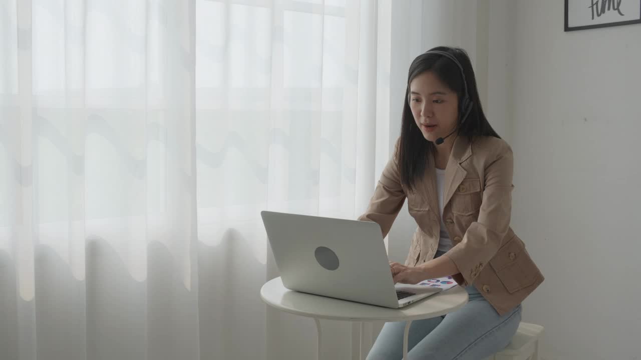 年轻的亚洲商业女性使用笔记本电脑进行在线视频会议，商业女性使用视频电话进行会议和显示财务、通信概念的图表报告。