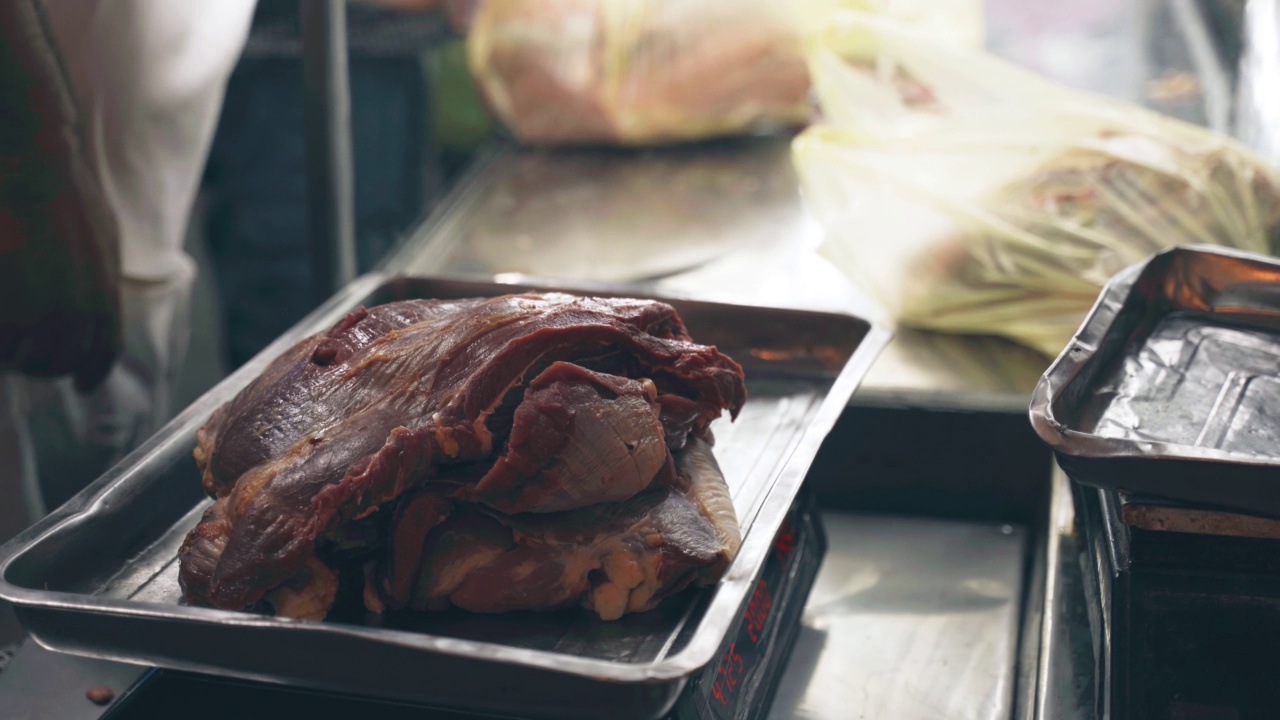 一名男子在街市上用秤称肉块的重量。