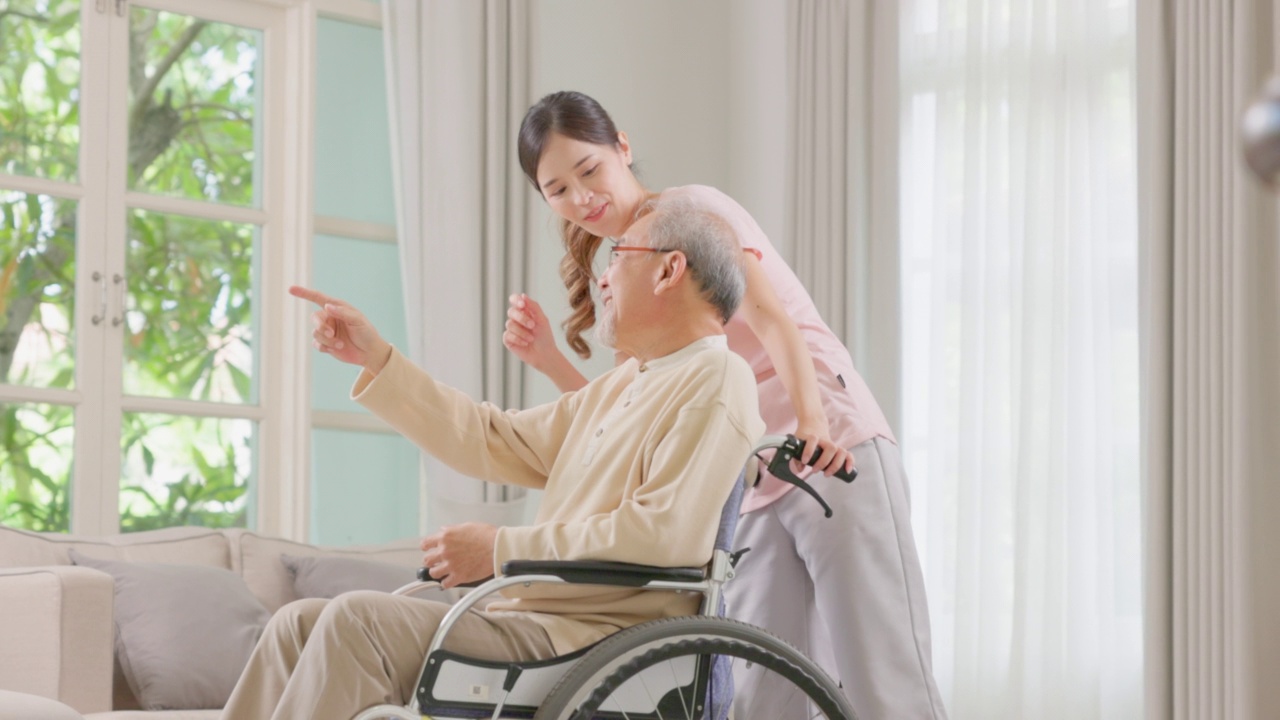 一位年长的男性病人坐在轮椅上，由一位年轻的女护理人员支持和协助。照顾者正在和一个心满意足的老人交谈