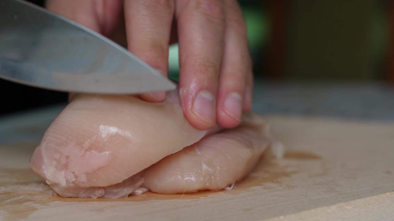 切板上的鸡肉片。男子用刀将精致的火鸡片切在砧板上。厨师切鸡胸肉，生白肉，厨师煮鸡胸肉，饮食健康饮食。