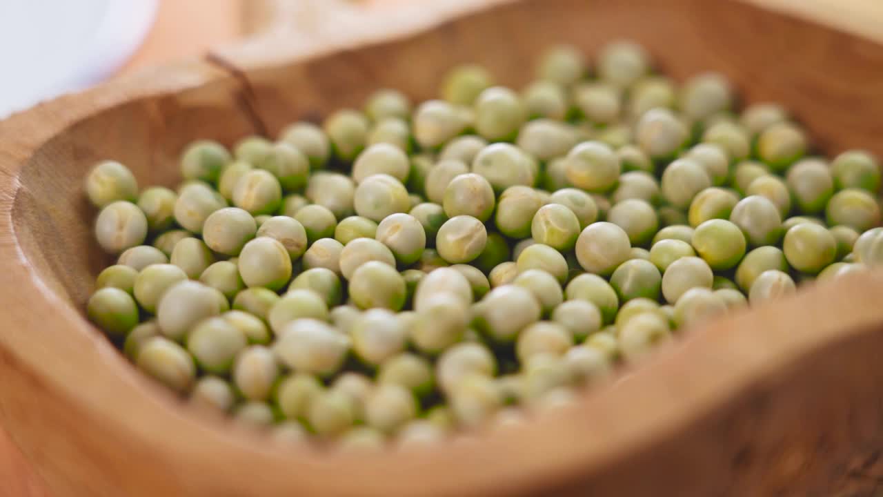 美味的整粒干绿豌豆掉进木碗里