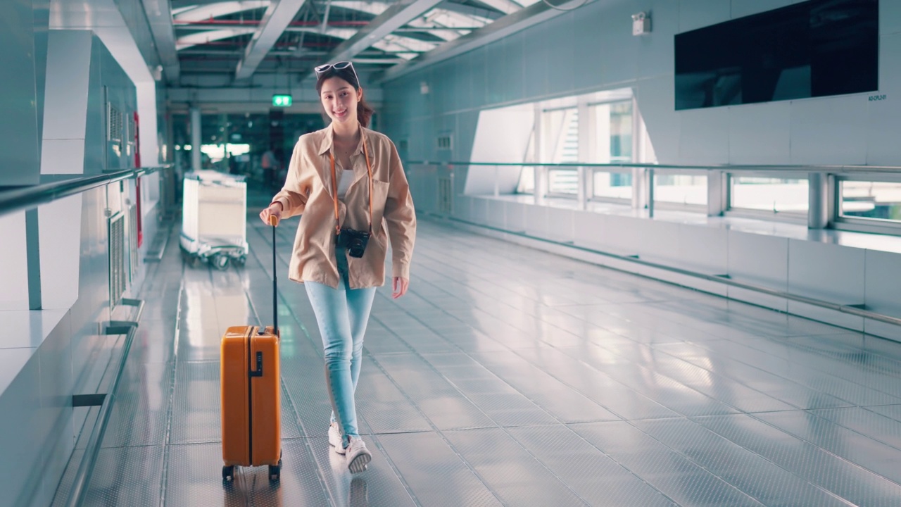 幸福微笑的亞洲女旅客走在機(jī)場(chǎng)候機(jī)樓行李箱行李。