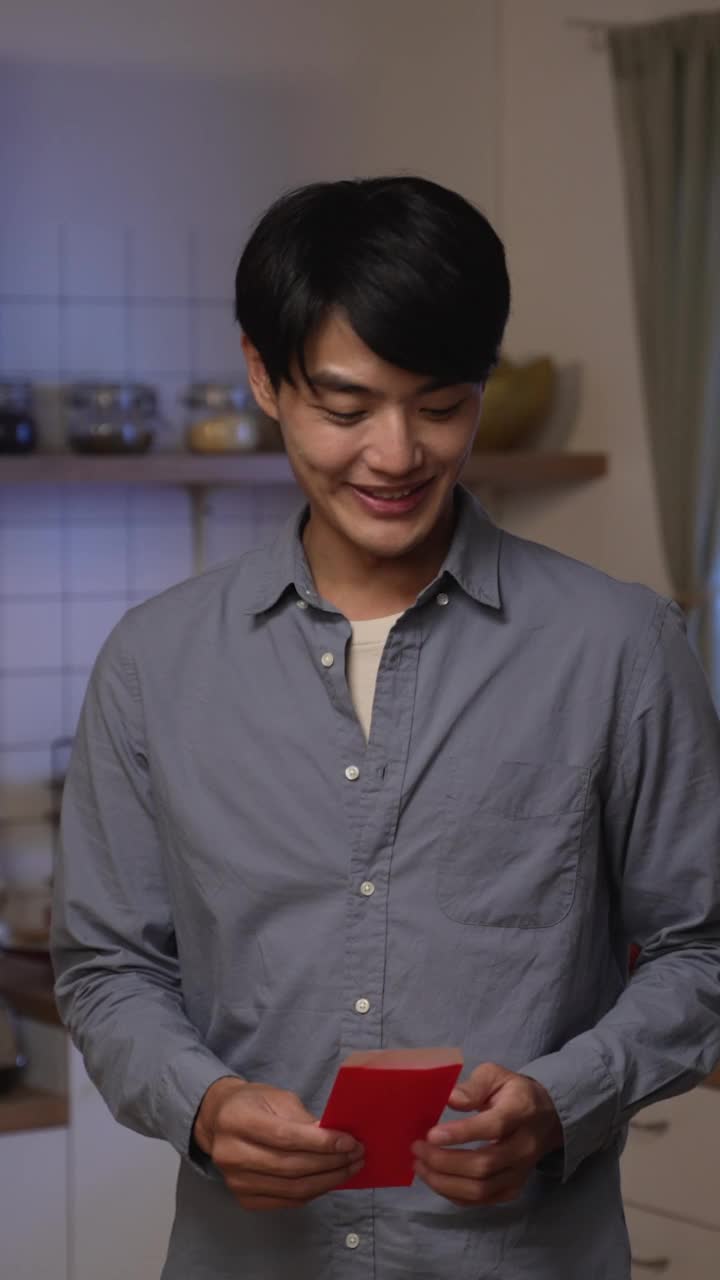 垂直屏幕:感恩的年轻夫妇给他们的年夜饭后在厨房里忙着的尴尬的老母亲红包压岁钱。单词翻译:财富