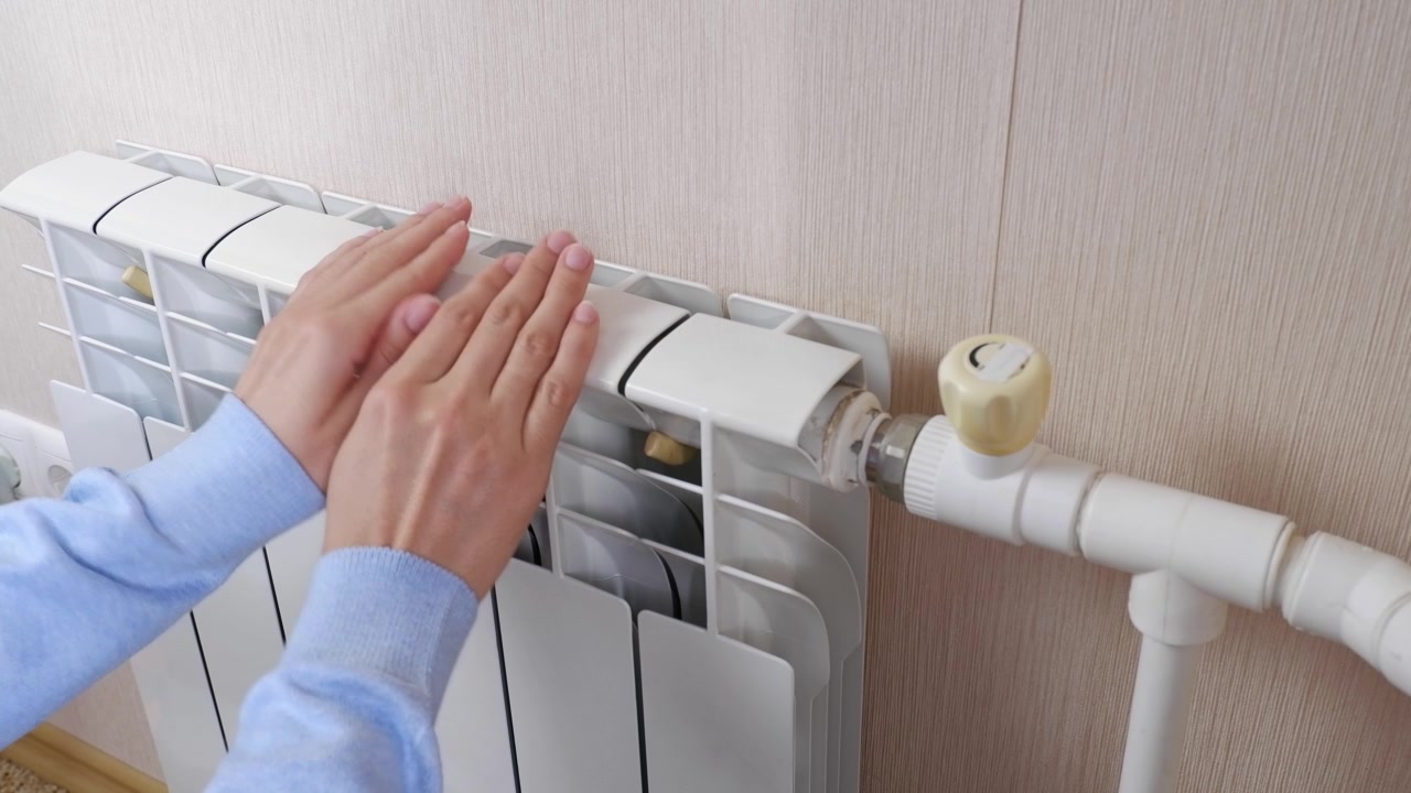 詳情圖-一名女性在家里的房間里用電池和加熱器取暖。手指，手掌保持暖氣片的溫度，靠近。室溫較低。冬季取暖期、季節(jié)。