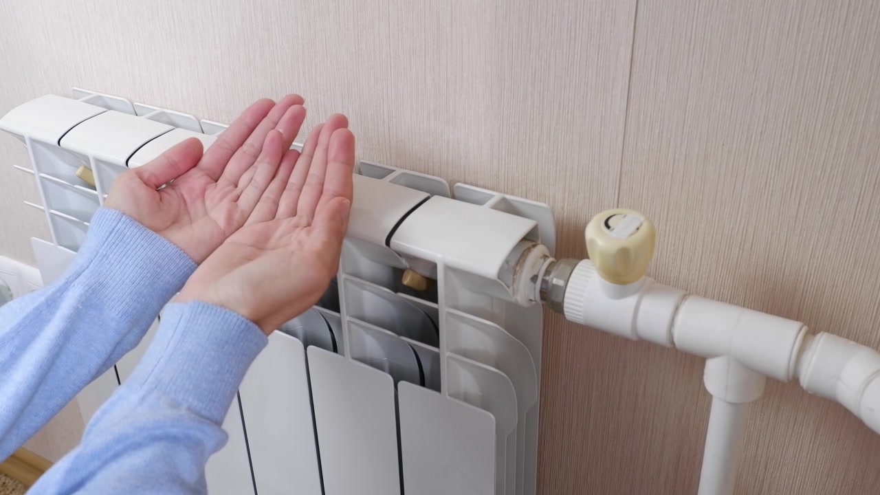 詳情圖-一名女性在家里的房間里用電池和加熱器取暖。手指，手掌保持暖氣片的溫度，靠近。室溫較低。冬季取暖期、季節(jié)。